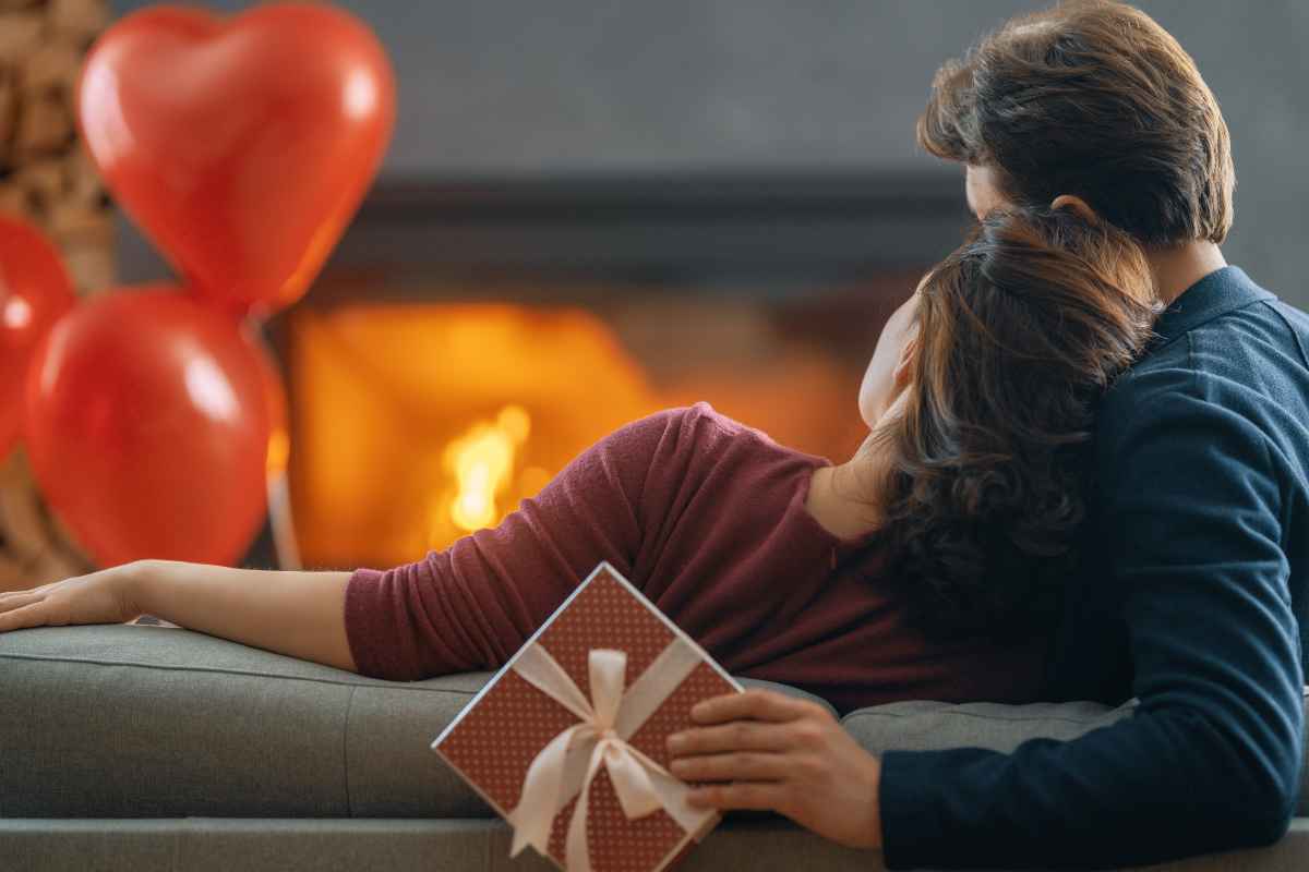 Coppia seduta sul divano davanti a un camino acceso con palloncini rossi